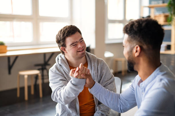 A young happy man with Down syndrome and his mentoring friend celebrating success indoors.